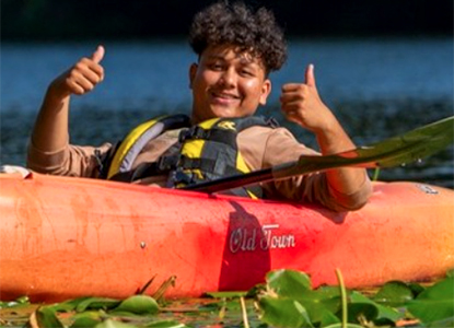 Hartwick College student in kayak smiling with thumbs up