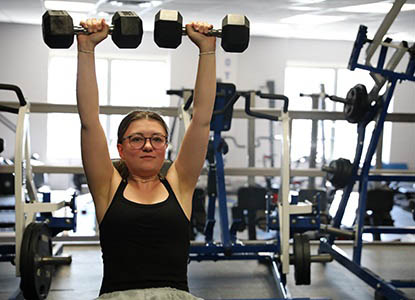 Hartwick College student in weight room lifting weights